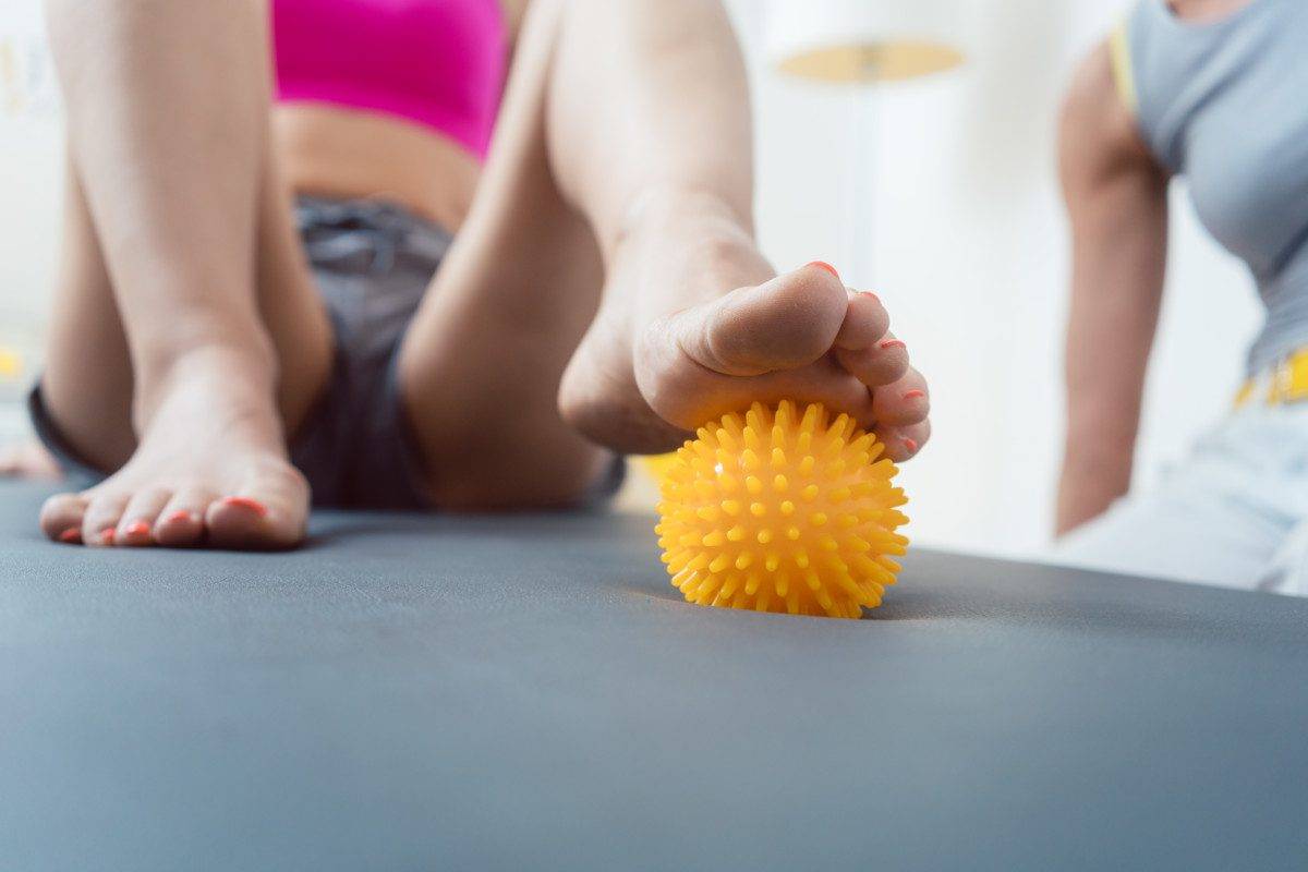 Woman rolling spiked ball under her feet in physical therapy