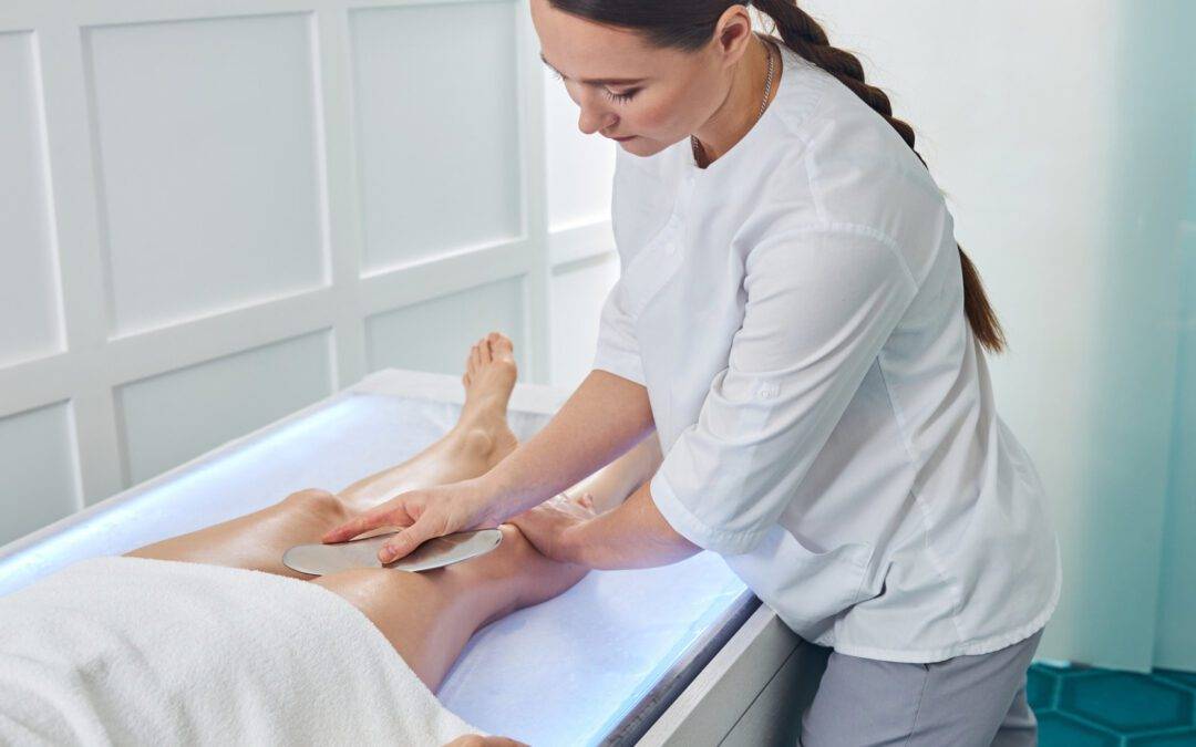 Physical therapist massaging woman leg with medical massager