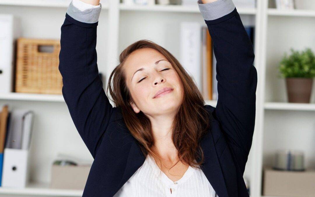 businesswoman stretching her arms above her head and smiling in pleasure as she sits behind her desk working