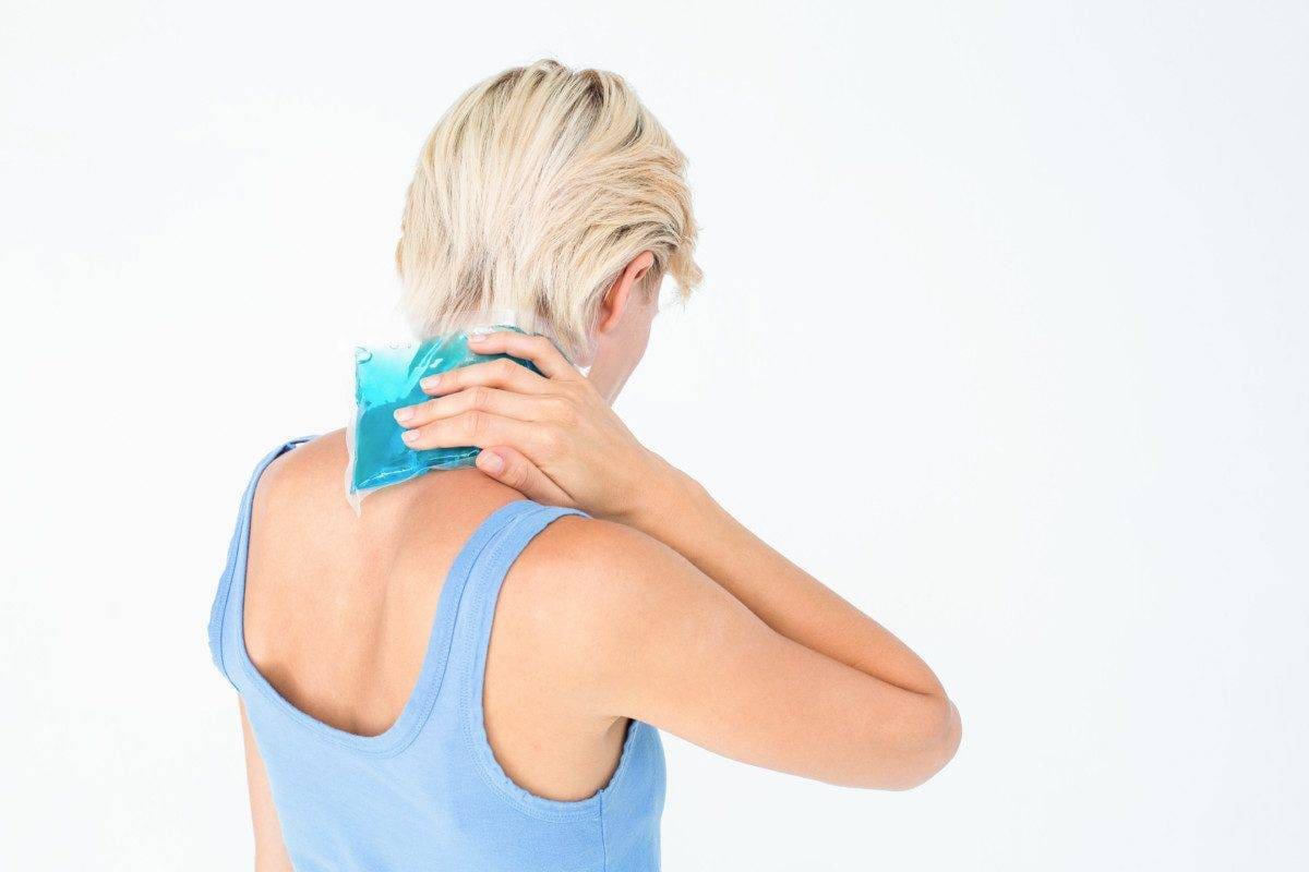 Blonde woman putting gel pack on neck on white background