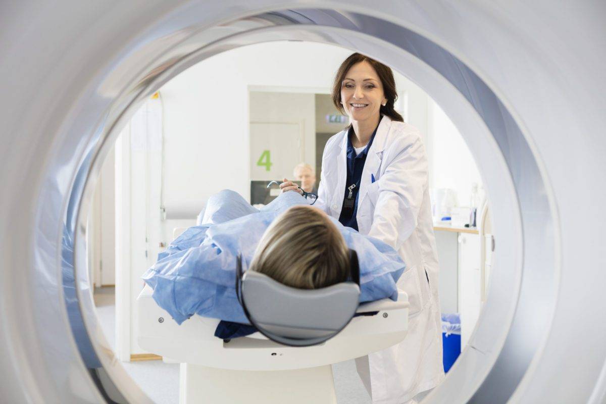 smiling female doctor looking at patient undergoing ct scan in hospital