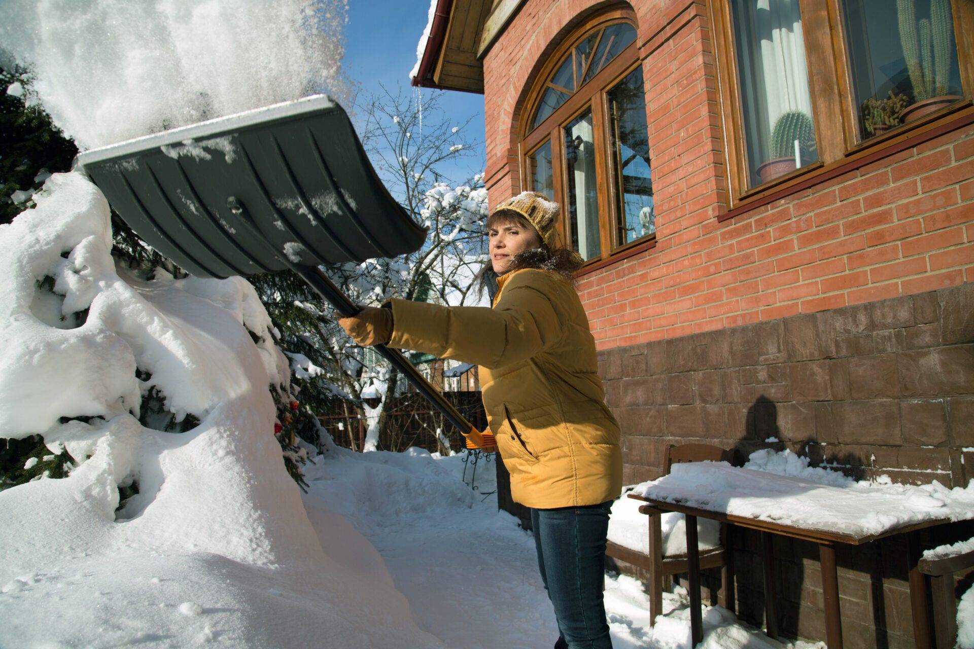 A woman throws snow with a shovel near the house