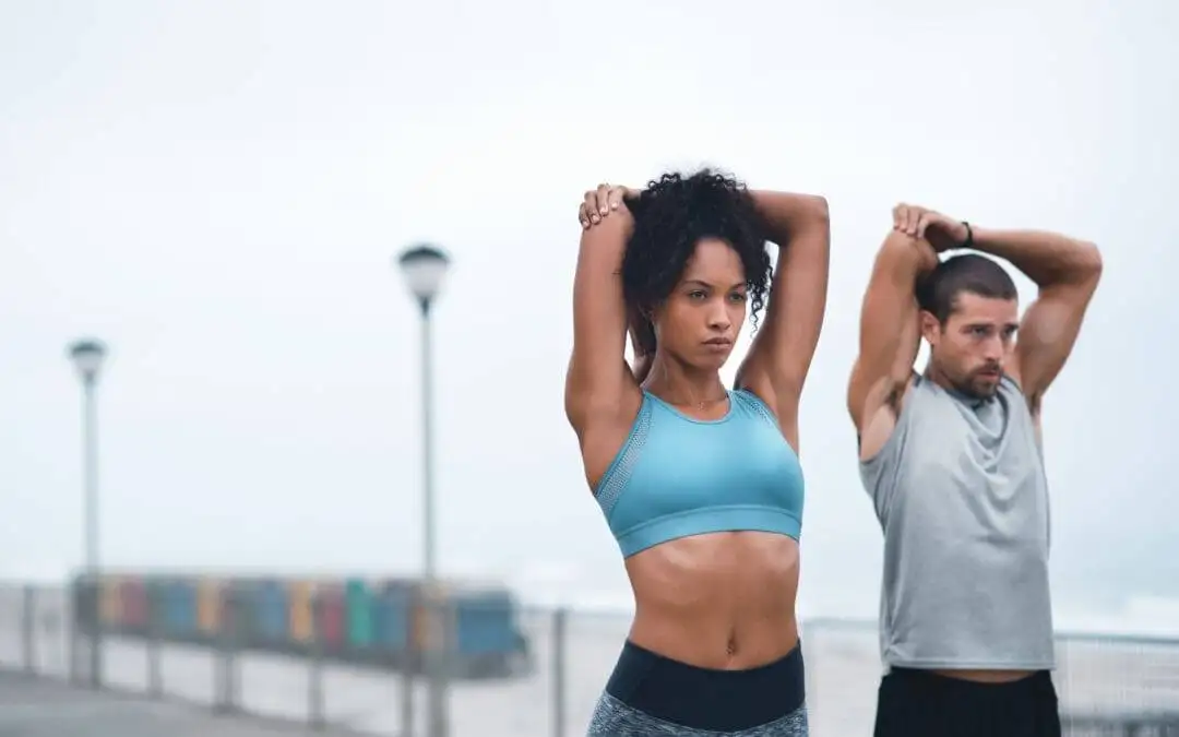 Two people stretching arms outdoors by waterfront